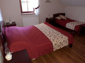 A bedroom with two single beds, a radiator, a window with curtains, a bedside table with a lamp, and a wooden floor. - Merkez Guest House (Brezice)