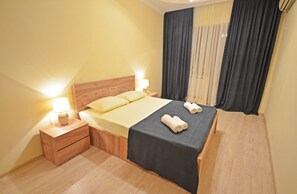 Une chambre d’hôtel avec un lit en bois, une table de chevet avec une lampe et une fenêtre avec des rideaux.