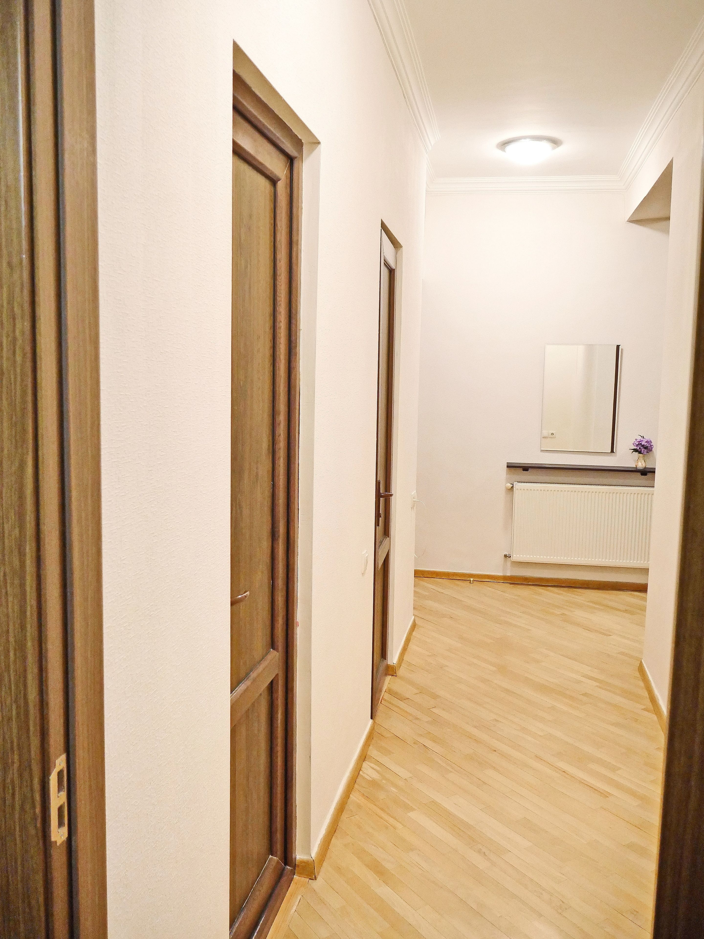 A hallway with wooden doors, a white wall, and a radiator.