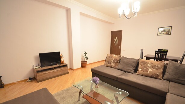 A living room with a sofa, a glass coffee table, a television, and a dining table with chairs.