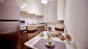 Une cuisine moderne équipée d’un réfrigérateur, d’un four à micro-ondes et d’une cuisinière. On y trouve une table à manger, mise avec des tasses à thé et un vase de fleurs.