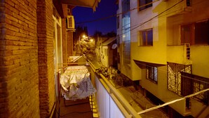 Une ruelle étroite avec un espace extérieur abrité où sont disposées des tables, un mur de briques et des bâtiments adjacents dotés de balcons et de garde-corps.
