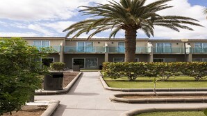 A building with a central courtyard, palm trees, and a pathway leading to the entrance. - Bungalows Corinto II (San Bartolome de Tirajana)