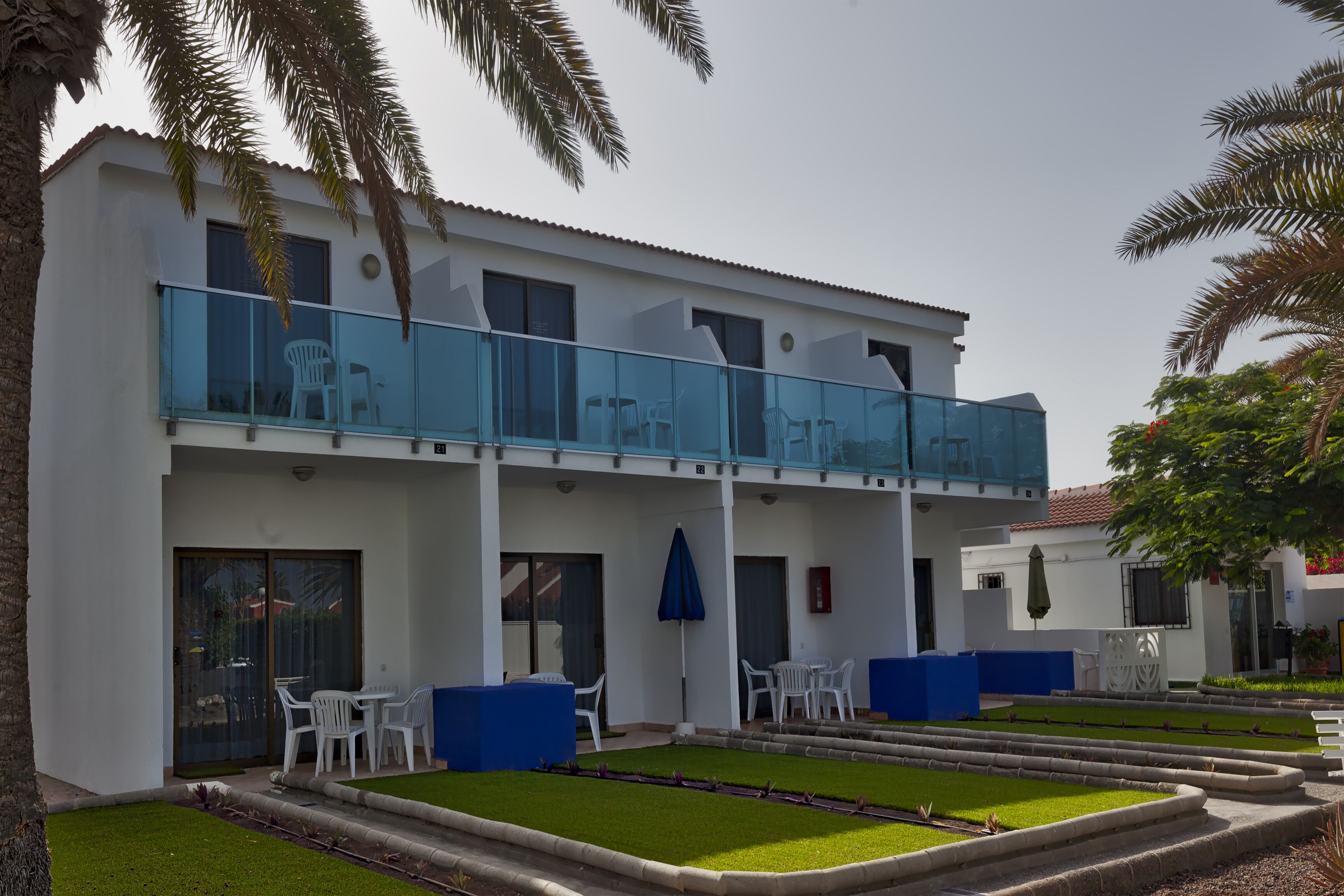 A two-story building with a balcony, white exterior walls, and a well-maintained lawn.