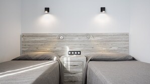 A bedroom with two single beds, a wooden headboard, bedside lamps, and a nightstand with a power outlet. - Bungalows Corinto II (San Bartolome de Tirajana)