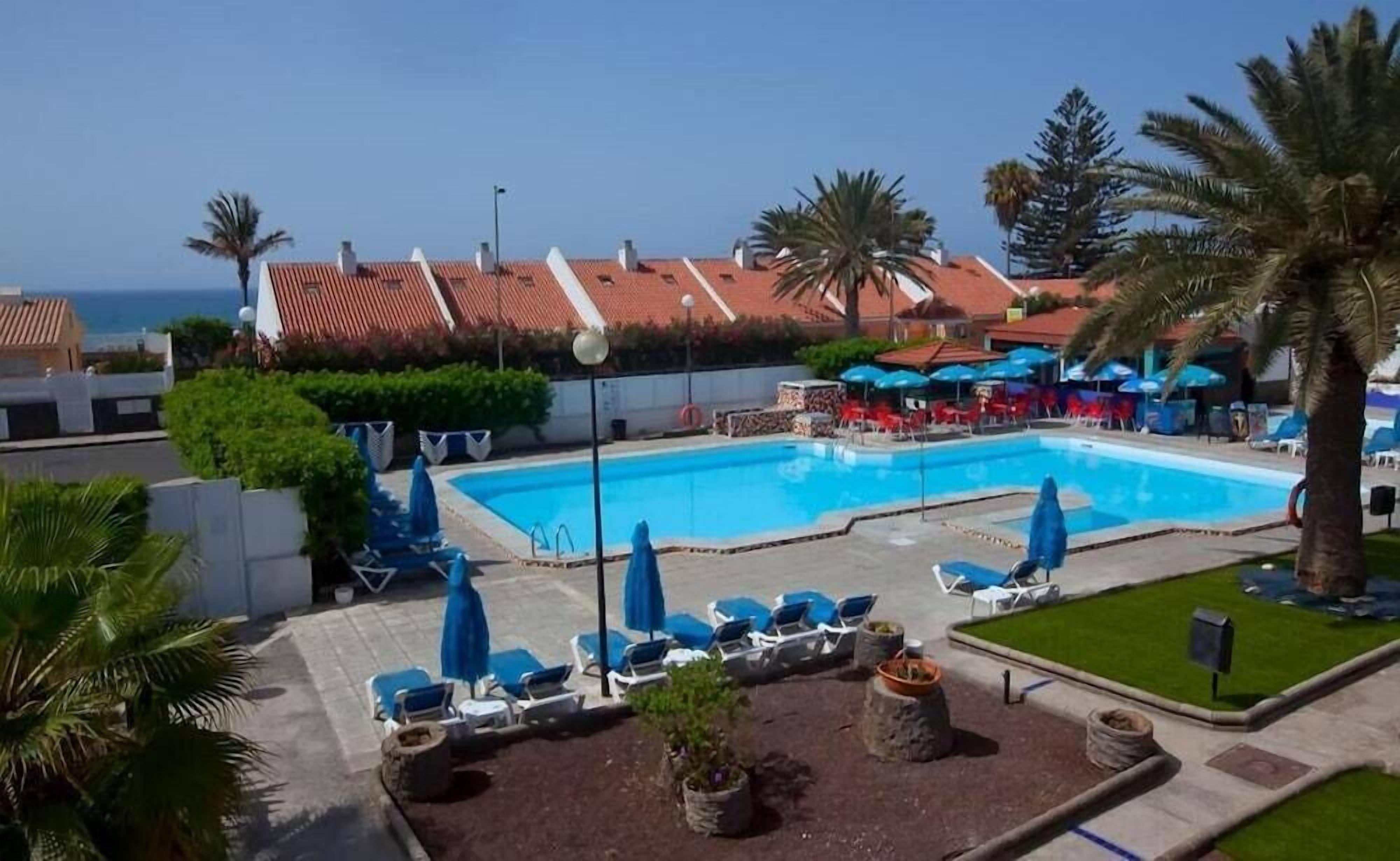 A swimming pool with lounge chairs and umbrellas, surrounded by greenery and a view of the sea.