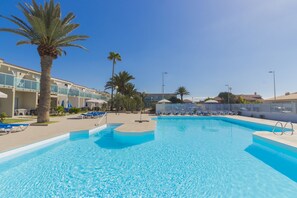 Una piscina azul cristalina con sillas de descanso y palmeras, rodeada de edificios de hotel.