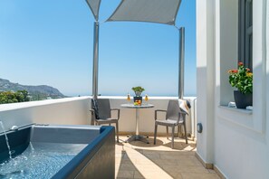 Een balkon met een hottub, twee rieten stoelen, een tafeltje met een bloempot en uitzicht op zee.