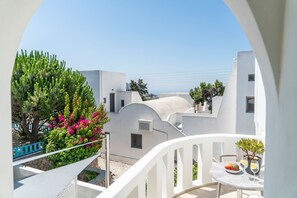 A white building with a balcony, a table with a fruit bowl and glasses, and a view of the sea. - Ladas Pyrgos (Santorini)