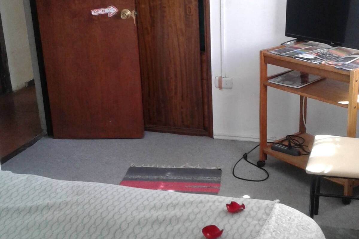 A room with a bed, a wooden wardrobe, a desk with a computer, and a television.