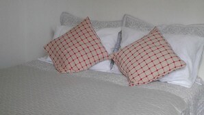 A bed with a white bedspread and two red and white patterned pillows. - Habitaciones Florencia La Serena (La Serena)
