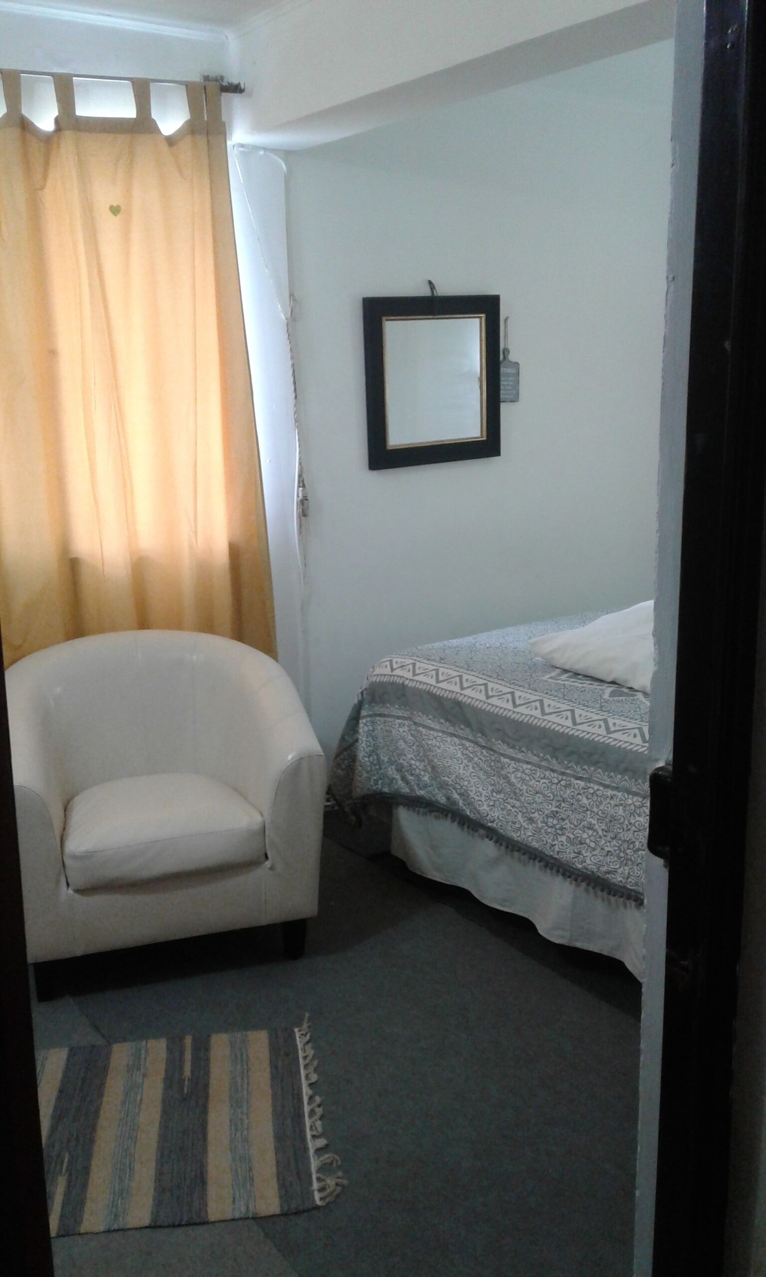 Une petite pièce, de taille modeste, comprenant un lit simple, une chaise et un tableau encadré accroché au mur.