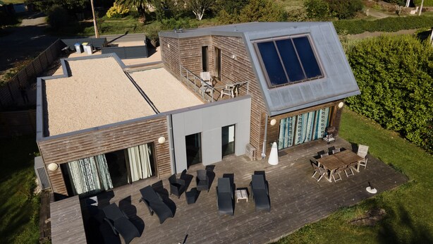 A modern house with a large deck, outdoor seating, and a solar panel on the roof.