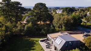 A modern house with a sloped roof, a deck with outdoor furniture, and a view of the sea.