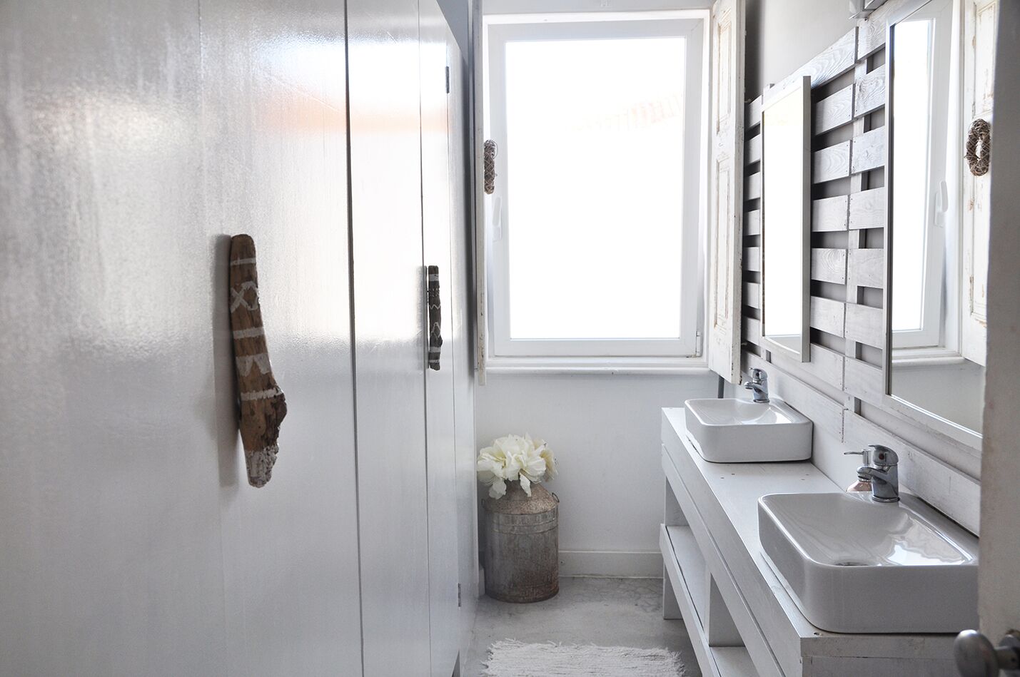 A bathroom with white cabinetry, a window, two sinks, and a mirror.