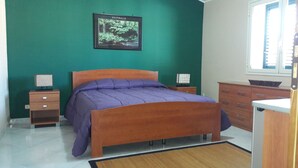 A bedroom with a wooden bed, a green wall, a framed picture of Australia, a nightstand, a dresser, and a window. - Palace Bed & Breakfast (Salaparuta)
