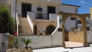 A building with a staircase leading to a balcony, a sign indicating a restaurant, and a stone archway. - Palace Bed & Breakfast (Salaparuta)