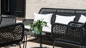 A wicker outdoor seating area with a table and chairs, a potted plant, and a white wall in the background. - La Pietra B&B (Grottazzolina)