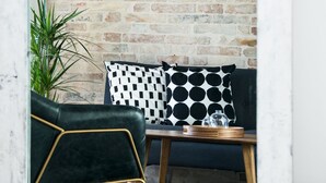 A cozy seating area with a brick wall, a green upholstered chair, a wooden table, and a patterned pillow. - La Pietra B&B (Grottazzolina)
