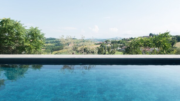 A clear swimming pool with a view of a green landscape and distant buildings. - La Pietra B&B (Grottazzolina)