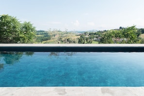 A clear swimming pool with a view of a green landscape and distant buildings. - La Pietra B&B (Grottazzolina)
