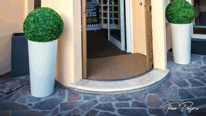 Ein Hotel mit gewölbtem Eingang, einem Schild mit der Aufschrift "ALBERGO NUOVO LONGATO" und zwei großen, geschnittenen Topfpflanzen.