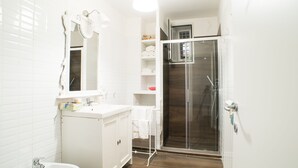 Ein Badezimmer mit weißem Waschbecken, Spiegel und Schrank, einer Dusche mit Glastür und einem weißen Handtuchhalter.