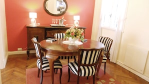 Un comedor con una mesa redonda de madera, seis sillas a rayas, un jarrón con flores y un espejo en la pared.