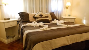 Una cama bien tendida con una colcha a rayas marrones y blancas, dos almohadas y un par de toallas sobre la cama. Hay dos mesitas de noche con lámparas, una a cada lado de la cama.