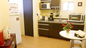 Cocina compacta con refrigerador, microondas, tostadora y un pequeño comedor con un florero.