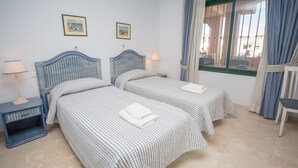 Une chambre avec deux lits, chacun recouvert d’une courtepointe à carreaux et agrémenté d’oreillers, une table de chevet avec une lampe et une fenêtre avec des rideaux.