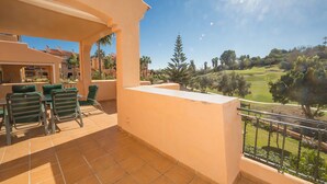 Un balcon donnant sur un terrain de golf, une terrasse avec des chaises et un bâtiment au sol carrelé.