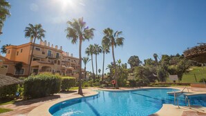 A pool with a curved edge, surrounded by palm trees and a building with balconies.