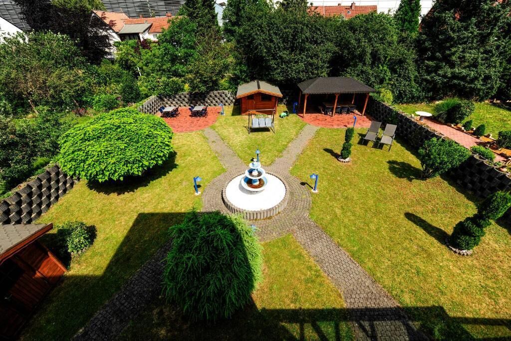 A courtyard with a central fountain, surrounded by a garden with various plants and a small wooden structure.