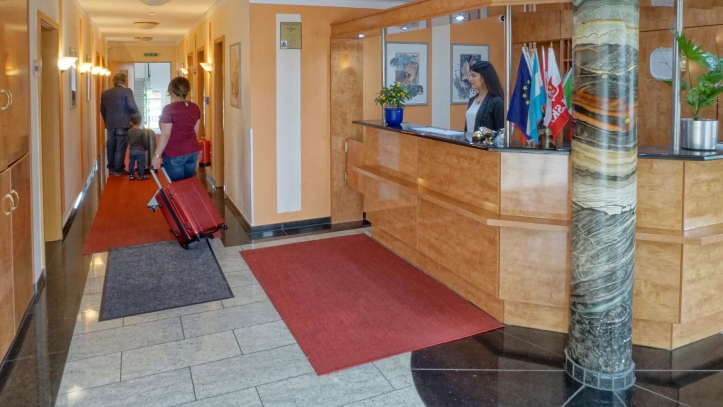 A hotel lobby with a reception desk, a red carpet, and a marble column.