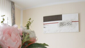 Een hotelkamer met een opgemaakt bed, een vaas met bloemen, een kopje en schoteltje, en een schilderij aan de muur.