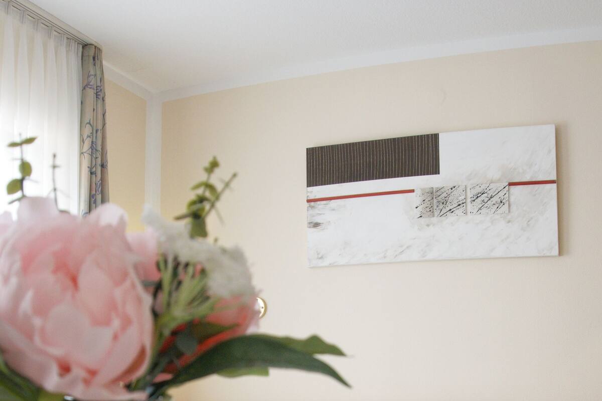 Ein Hotelzimmer mit einem ordentlich bezogenen Bett, einer Vase mit Blumen, einer Tasse und Untertasse sowie einem Bild an der Wand.