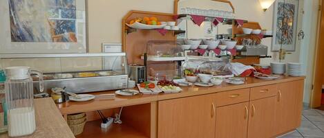 Una mesa de buffet con diversos alimentos, una estación de café y una vitrina de vidrio.