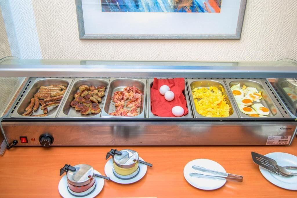 A buffet with various food options including sausages, bacon, eggs, and scrambled eggs.
