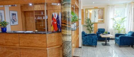 A reception area with a wooden counter, flags, a marble column, and blue seating.
