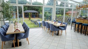 Een restaurant met glazen wanden, met uitzicht op een tuin en terrasplekken.