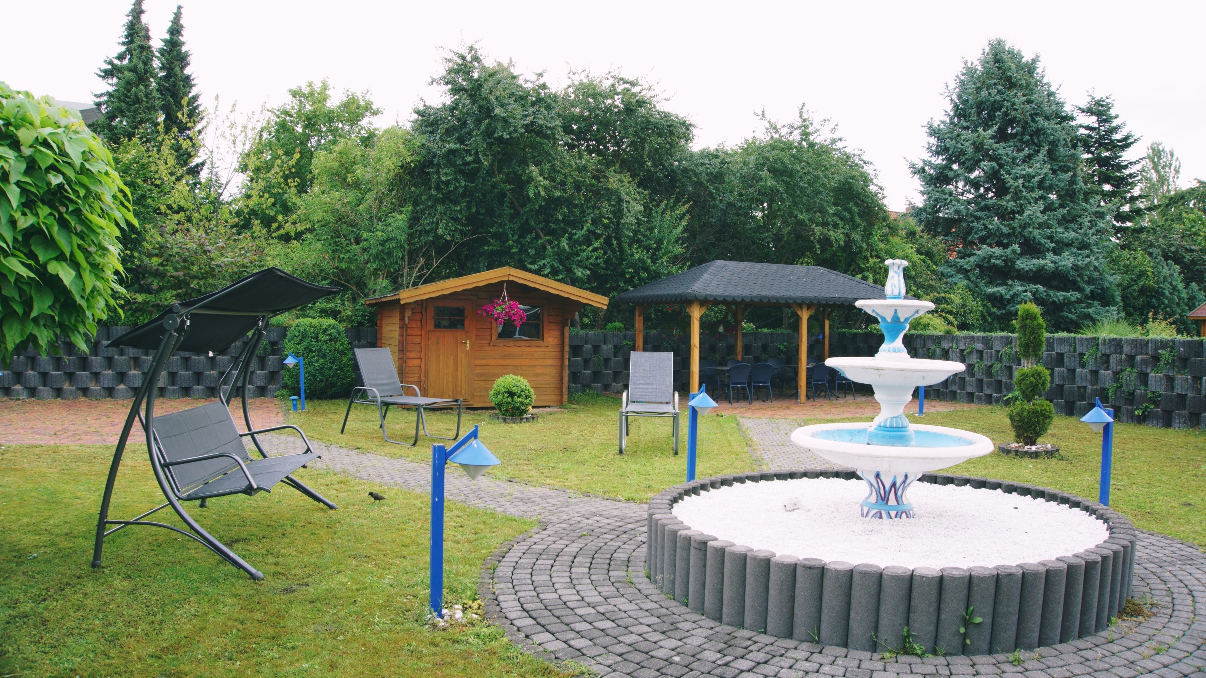 A garden with a circular fountain, a wooden playhouse, and a covered seating area.