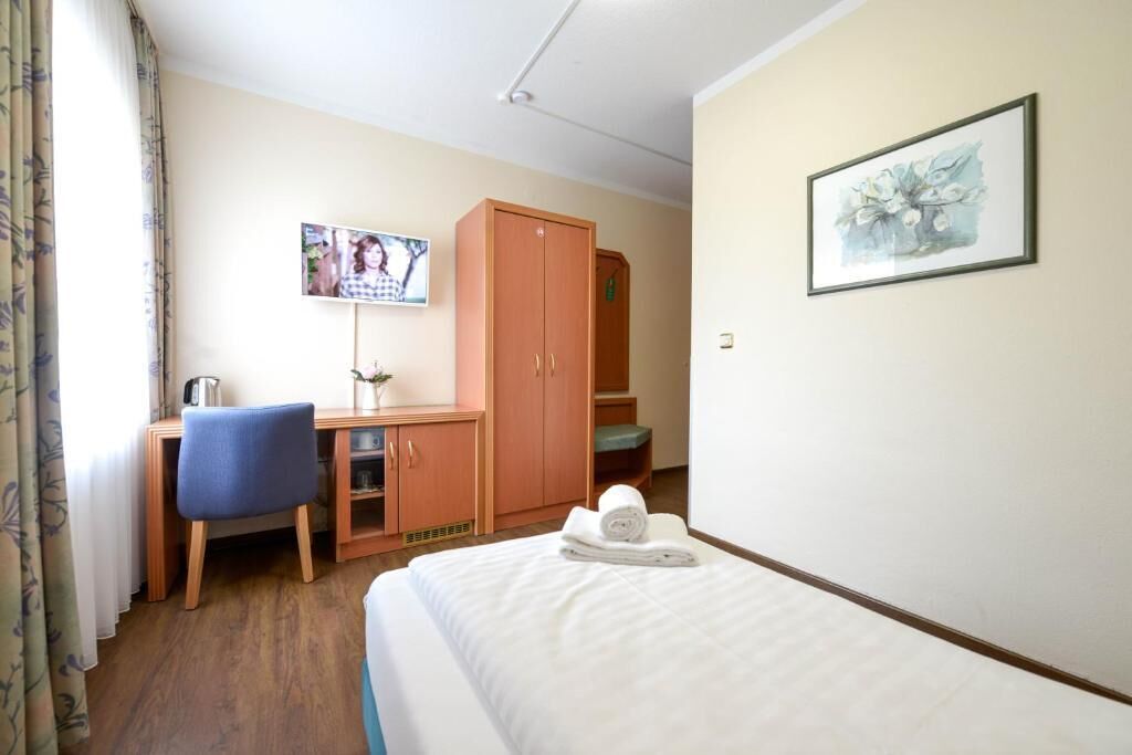 A hotel room with a bed, a desk, a chair, a wardrobe, a television, and a framed picture on the wall.