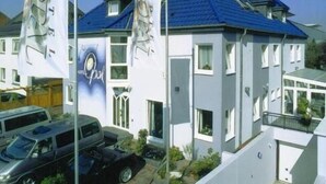 Een modern, tweelaags gebouw met een blauw dak, witte muren en veel ramen. Voor het gebouw staan twee vlaggen met tekst en afbeeldingen op vlaggenmasten.