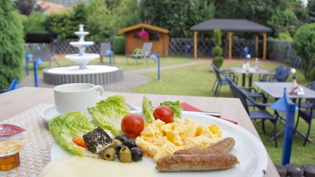 Een maaltijd op een tafel buiten, met uitzicht op een tuin, inclusief een prieel en een fontein op de achtergrond.