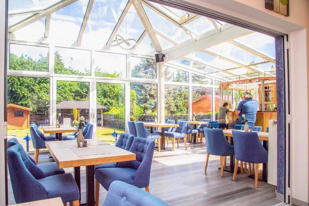 An indoor dining area with tables and chairs, large windows, and a view of the outside.