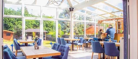 An indoor dining area with tables and chairs, large windows, and a view of the outside.