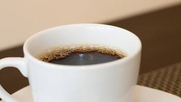 A white cup of coffee with a spoon on a white saucer.