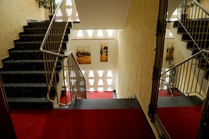 Una escalera con escalones negros y alfombra roja que conduce a una plataforma con dos cuadros.