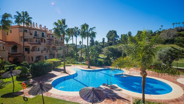 A resort with a large pool, palm trees, and a multi-story building with balconies.